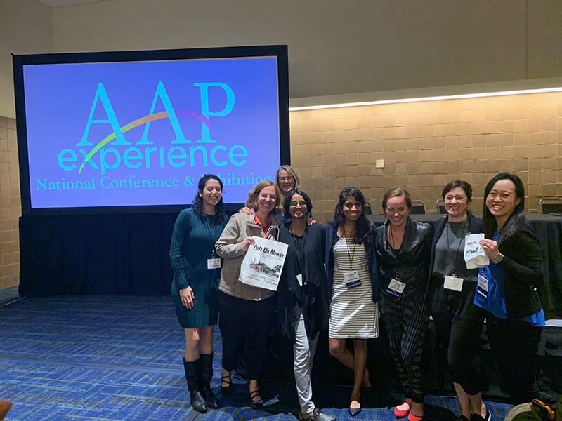 several people posing for a photo in a conference room with an AAP Experience sign behind them